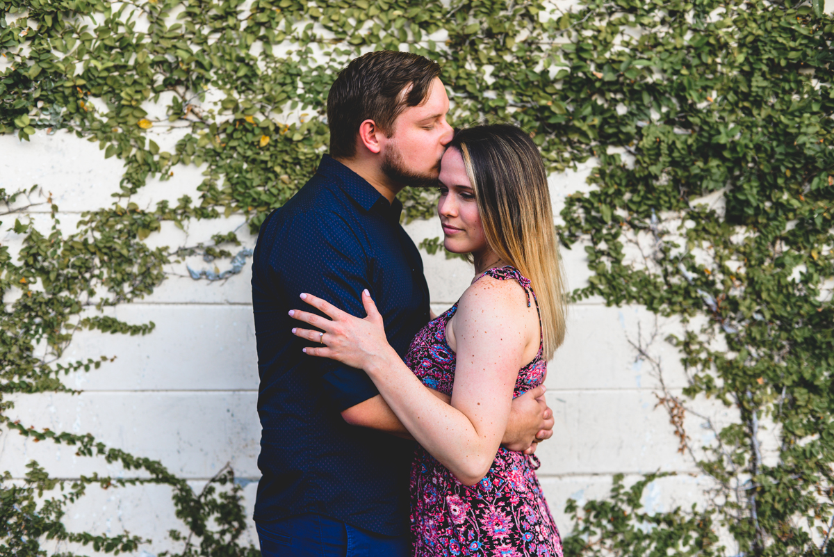 greenery, kissing, engaged, vines, leaves, brick, wall